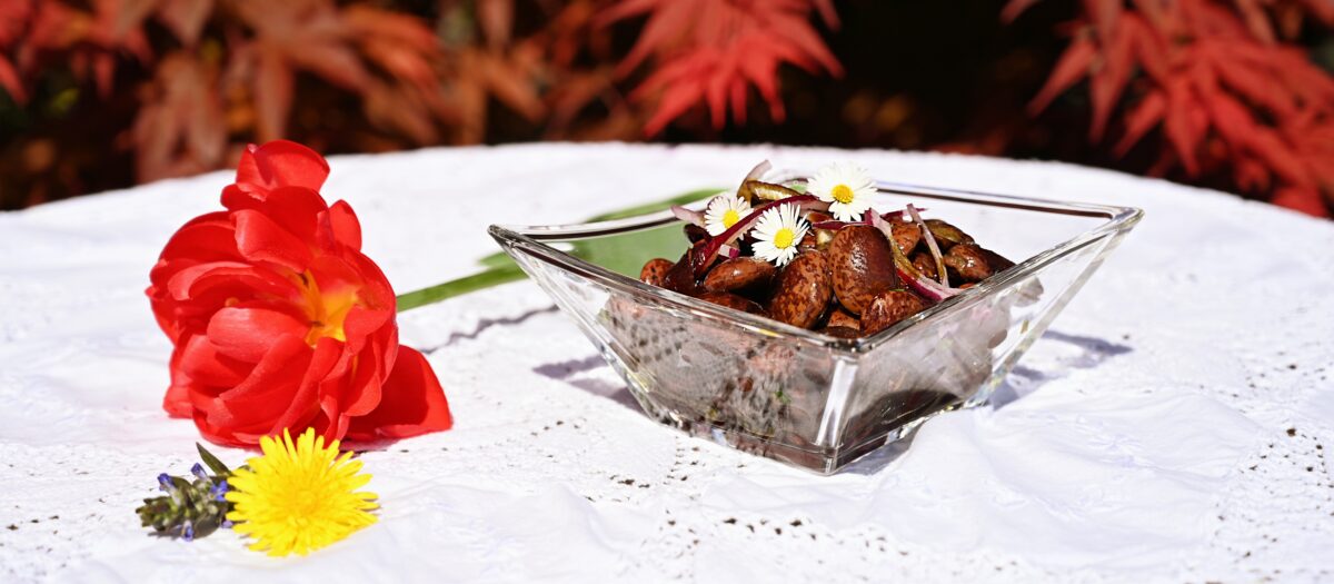 Steirischer Käferbohnensalat in einer Schale auf einem Tisch, dekoriert mit Blumen